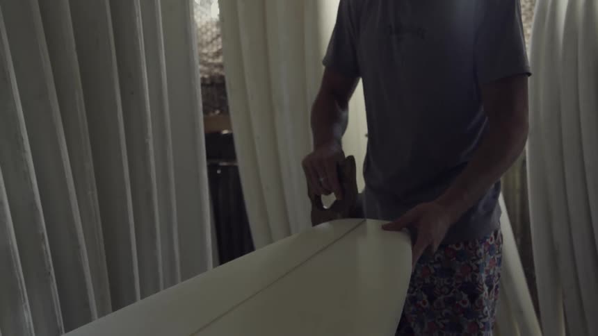 A man uses a saw to trim the end of a surfboard