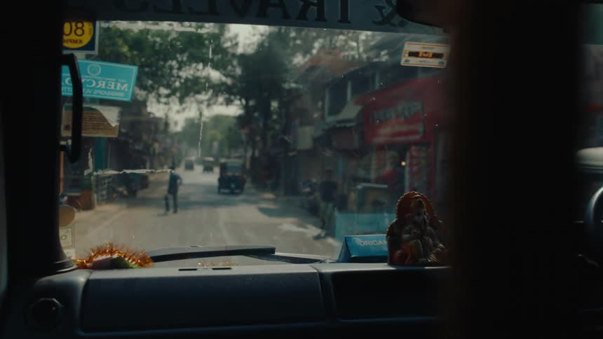 Inside a car with several cars motorcycles and houses visible on the street