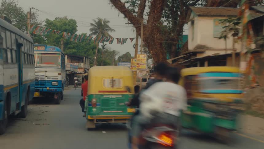 Heavy traffic including buses and auto rickshaws moves along a street passing through town during the daytime