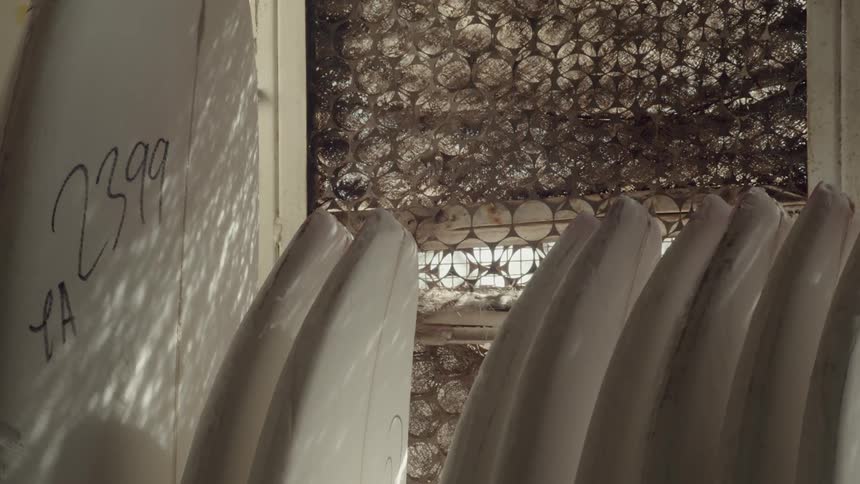 The sun shines through a covered window casting a pattern on unfinished surfboards in a shop