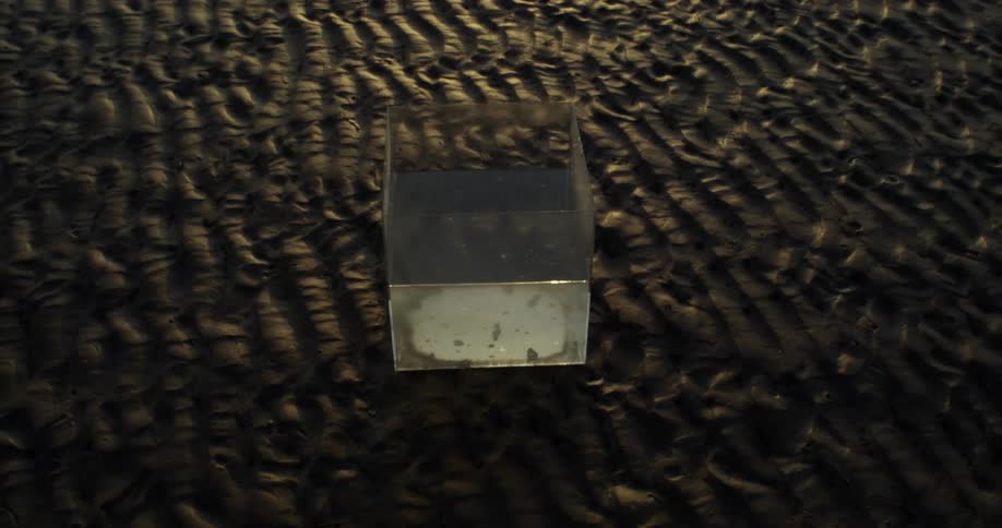 Glass container with water static on wet beach sand