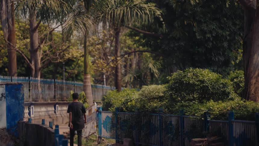 A person is walking alone through a park or garden pathway surrounded by dense greenery and trees