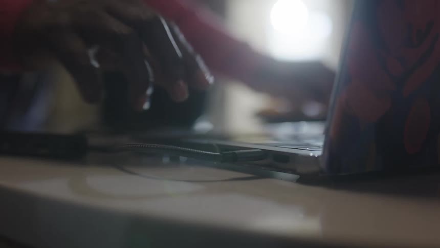 Pair of hands plugging a cable into a laptop and then starting to type