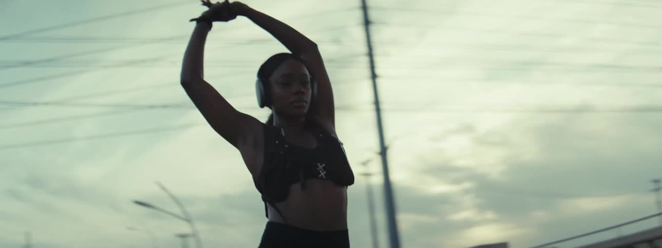 A woman wearing headphones stretches gracefully outdoors under moody skies exuding focus and determination in a wide shot
