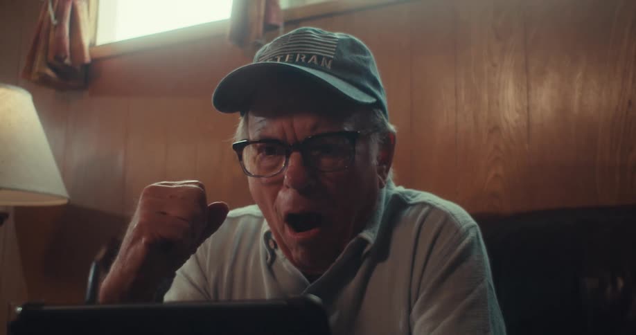 Elderly man sitting on the couch holding a tablet watching a game and cheering intensely