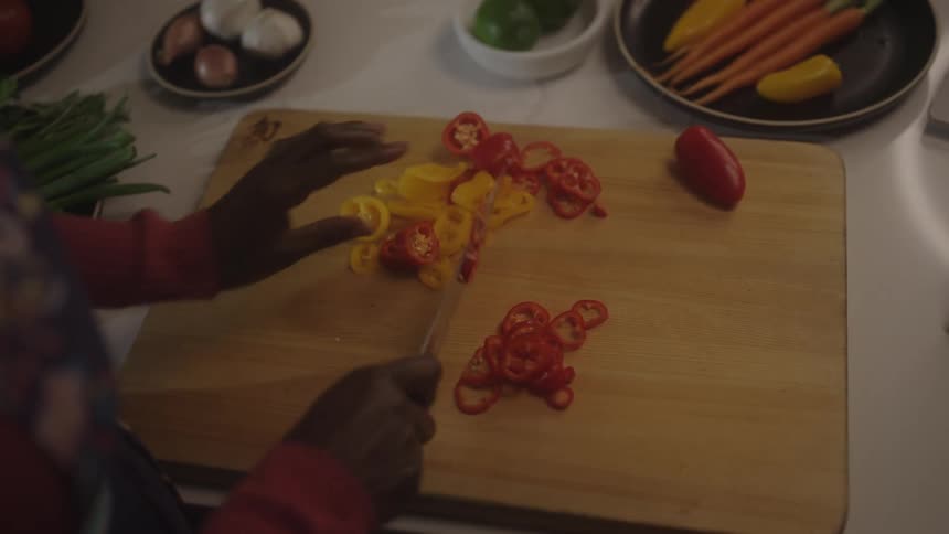 A woman slicing a tomato on a cutting board in the kitchen with a tablet placed on the right side