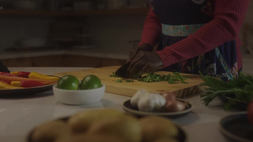 A black woman smells fresh herbs and chops them on a wooden cutting board