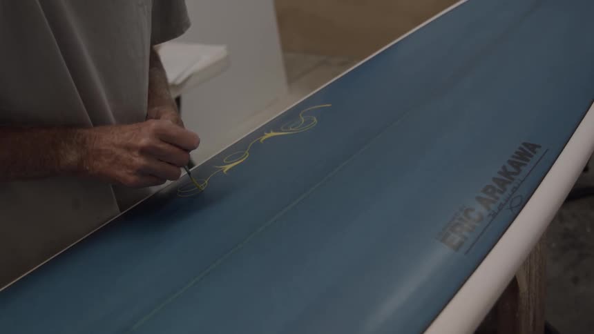 Man paints yellow design on a surfboard