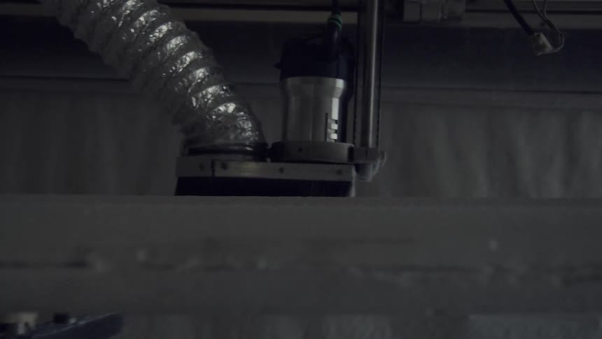 A factory machine runs over an unfinished surfboard