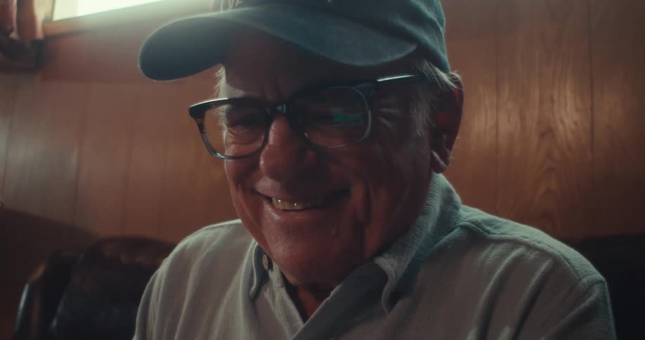 An elderly man sitting on the living room sofa smiling