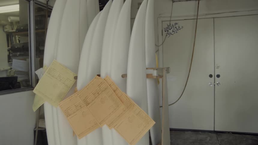Unfinished surfboards are stacked on a rack