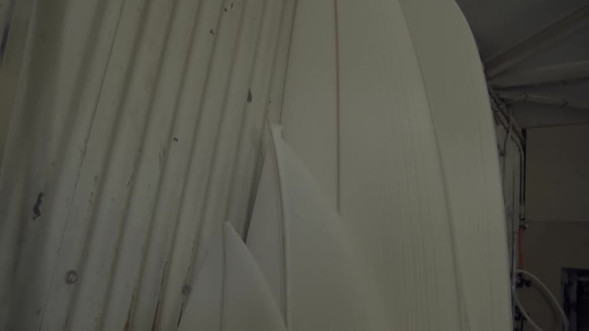 Unfinished surfboards line the interior of a warehouse during the day