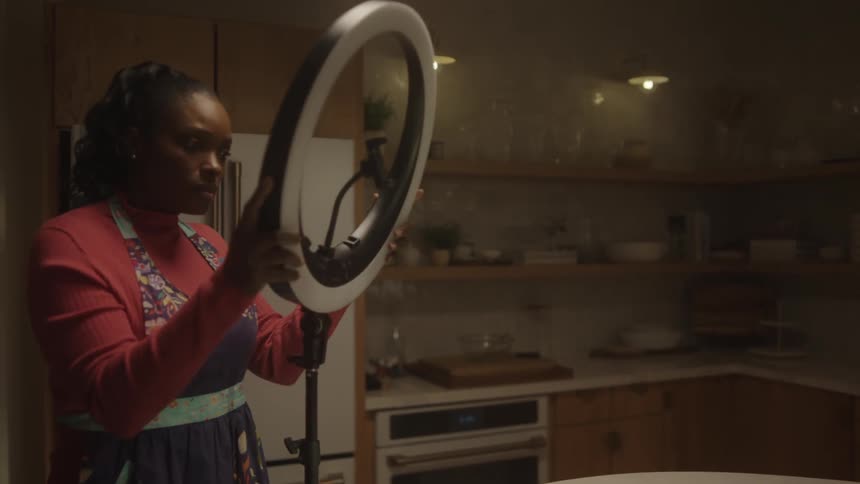A woman sets up lighting to begin filming herself cooking