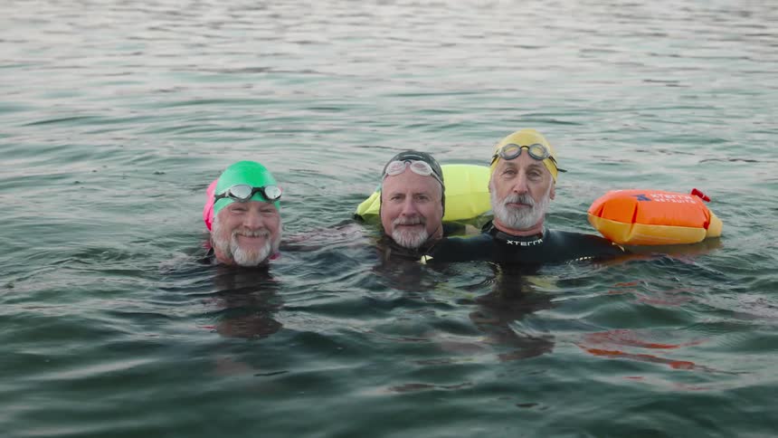 A group of swimmers float and smile in a water body