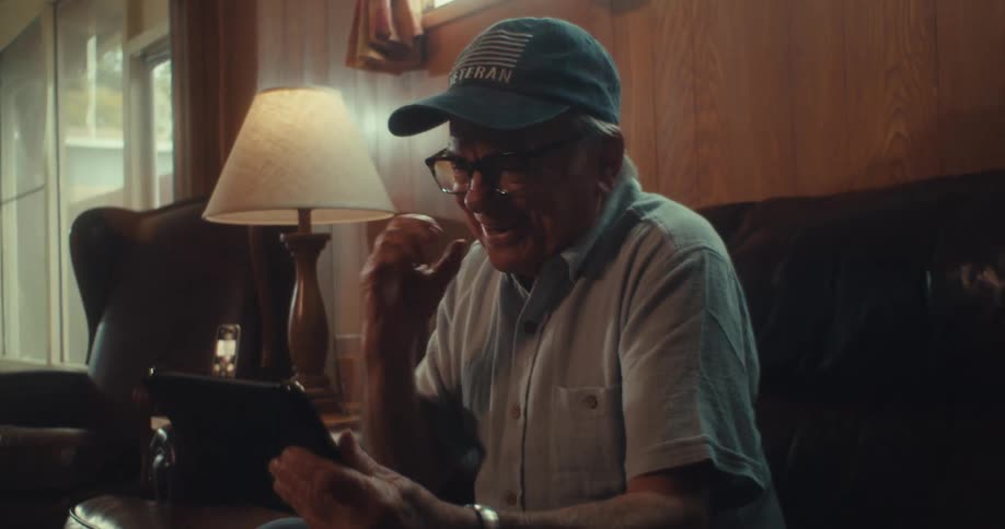 Elderly man celebrates while watching a competition on his tablet in his living room
