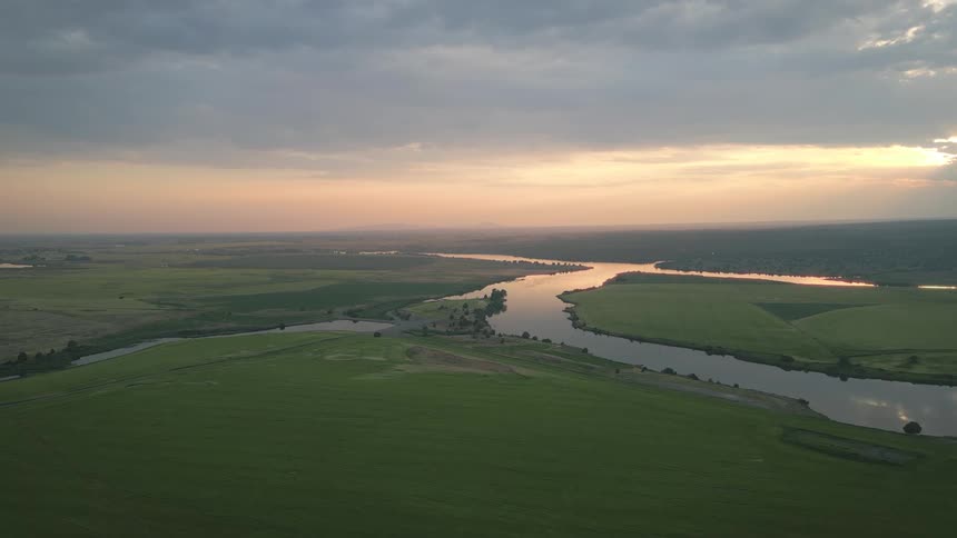 Aerial shot of a winding river in an area surrounded by vegetation and green farm fields
