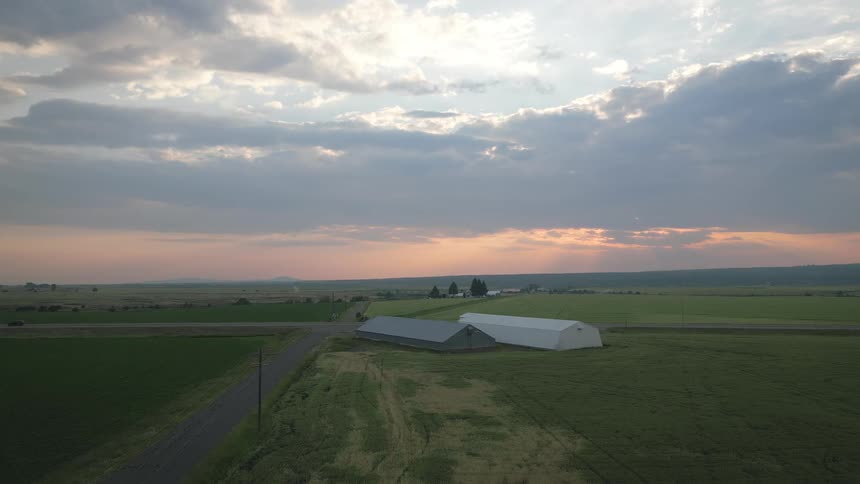 Aerial shot of two metal strucures in agricultural fields at sunrise