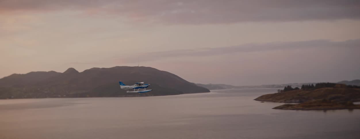 Single engine airplane flying above the ocean with mountains in the background