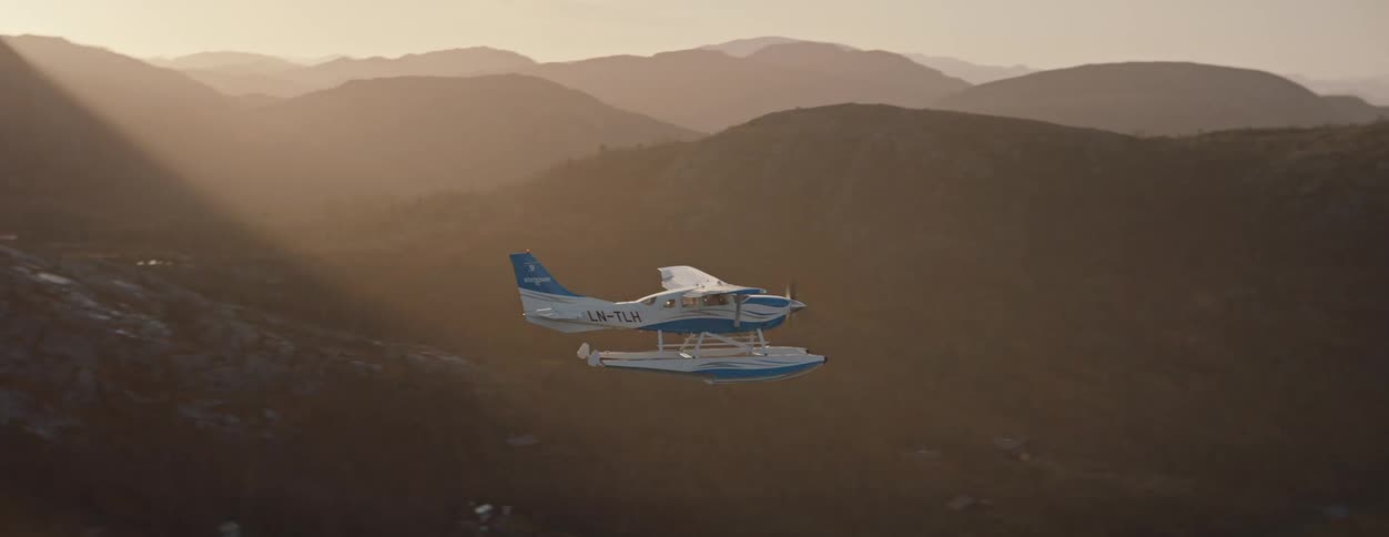 Seaplane flies through the sky over foggy mountainous terrain during the daytime