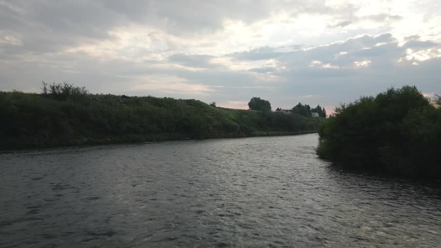 A wide river flows between lush banks under a cloudy sky