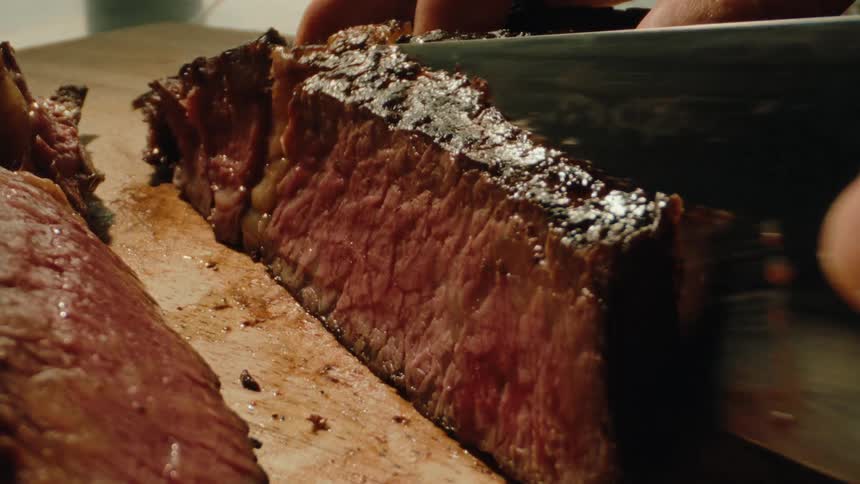 Closeup of a person cutting a piece of steak with a knife