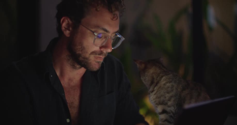 A man is typing on a tablet keyboard while a tabby cat sits beside him