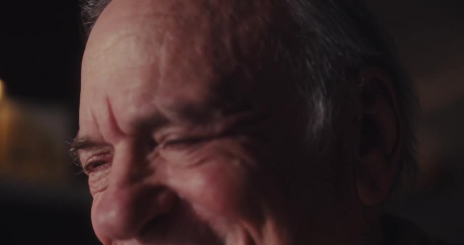 A closeup of an elderly man smiling warmly with soft lighting emphasizing the joy and texture of his expression