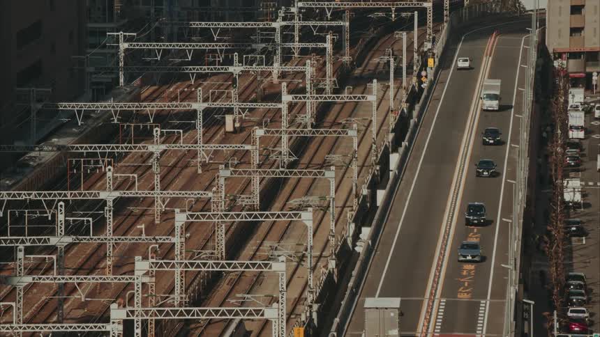 Train travels along one of multiple train tracks paralleling a busy highway while pedestrians walks on a nearby sidewalk
