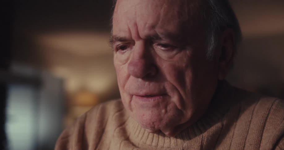 An elderly man with a concerned expression gazes intently at his laptop screen smiling afterward