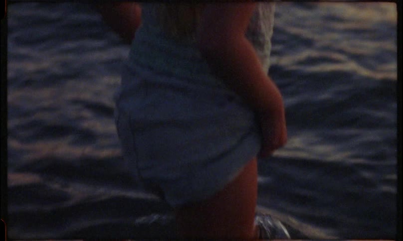 A young girl stands at the edge of the water contemplatively gazing at the ocean during sunset