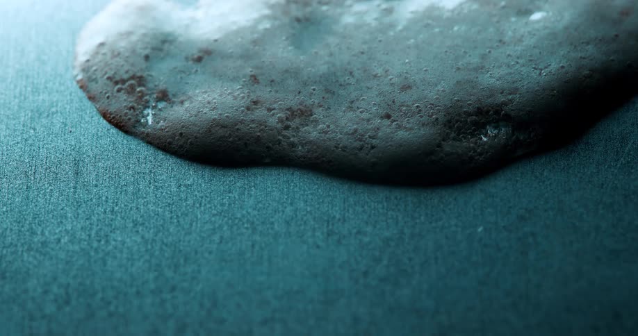 A foamy bubbly substance spreads across a textured blue surface with small bubbles forming throughout the foam