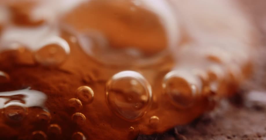 Golden brown bubbles on a glossy surface in an extreme macro shot highlighting surface tension and organic flow