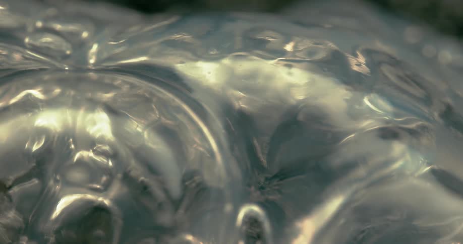 A golden bubble slowly forms and expands on a rippling glossy surface in an extreme closeup macro shot