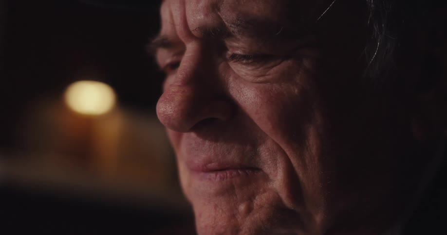 A tight closeup of an elderly mans contemplative expression softly lit in a warm intimate setting