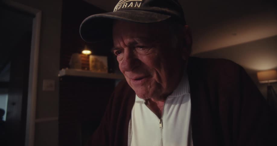 Elderly man sitting and wearing a cap with mixed emotions