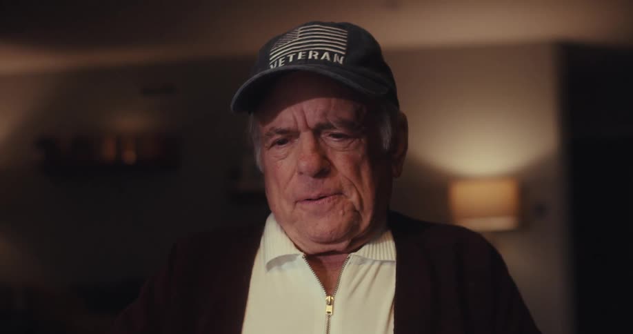 Elderly man wearing a cap in a room interacting with a laptop