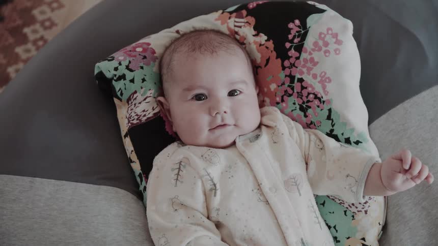 Lying baby in printed jumpsuit rests on colorful pillow with floral designs