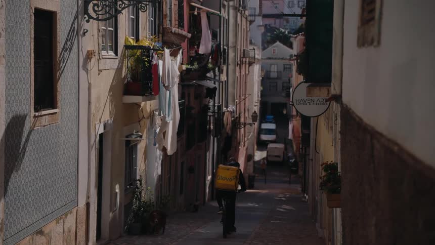 A person is riding a delivery bike down a narrow sloped alleyway at midday