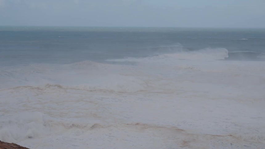 A tumultuous sea churns with white foam extending to a distant horizon under a gray sky