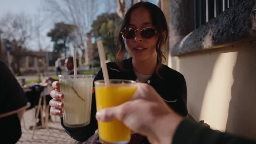 A man toasting with a woman at a table on the street they are drinking juice