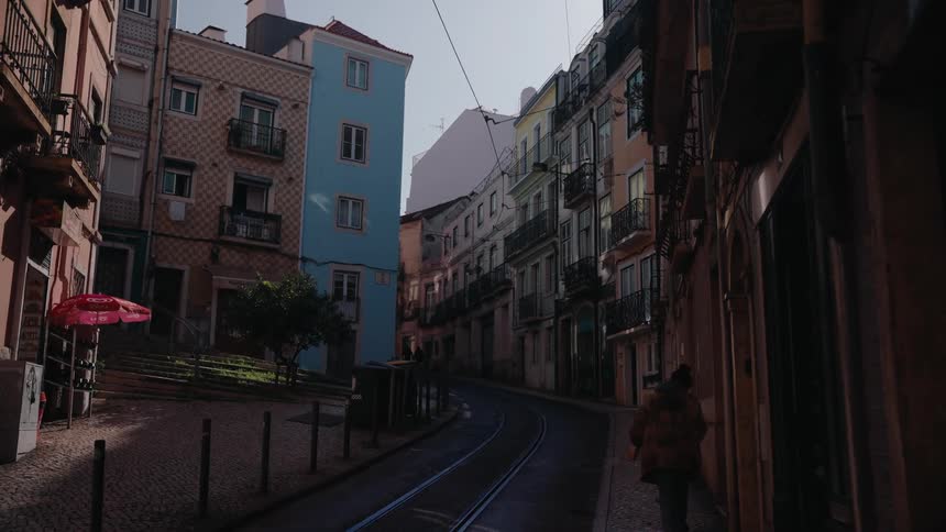 A narrow european street with colorful buildings and tram tracks as a person walks into the shadows
