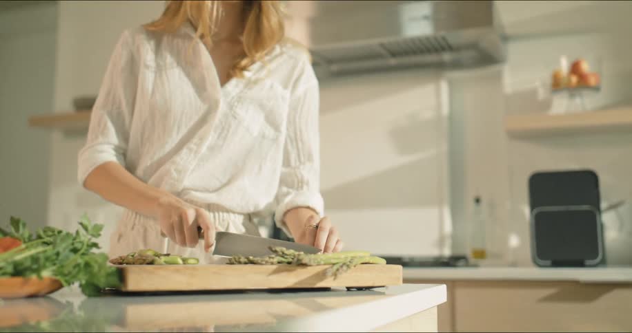 A woman in the kitchen cutting asparagus on a cutting board