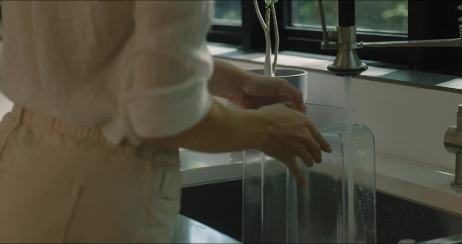 A woman in the kitchen washing a plastic container in the sink