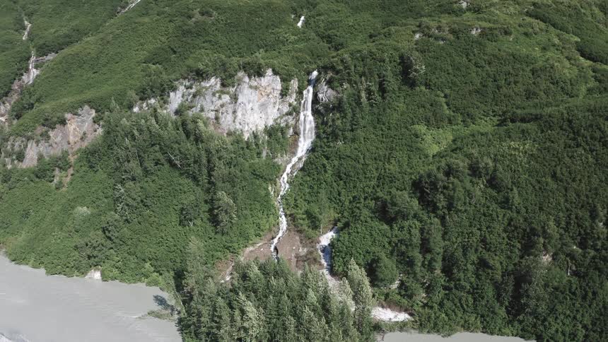 A powerful waterfall between mountains surrounded by many trees with a river below