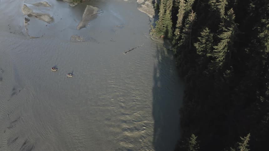 People in two small boats on a river surrounded by conifers