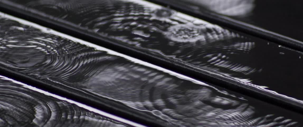 A close up of wet wooden planks with raindrops forming rippling concentric circles on the glossy surface