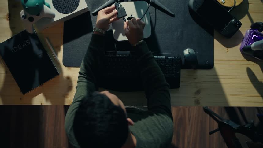 A young man sets up a compact desktop computer at a modern workstation surrounded by tech gadgets and creative tools