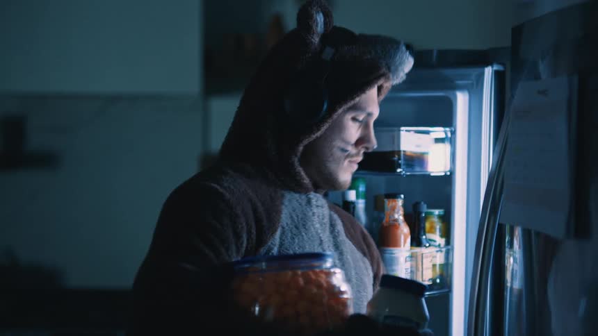 Man in a bear onesie getting food from the refrigerator