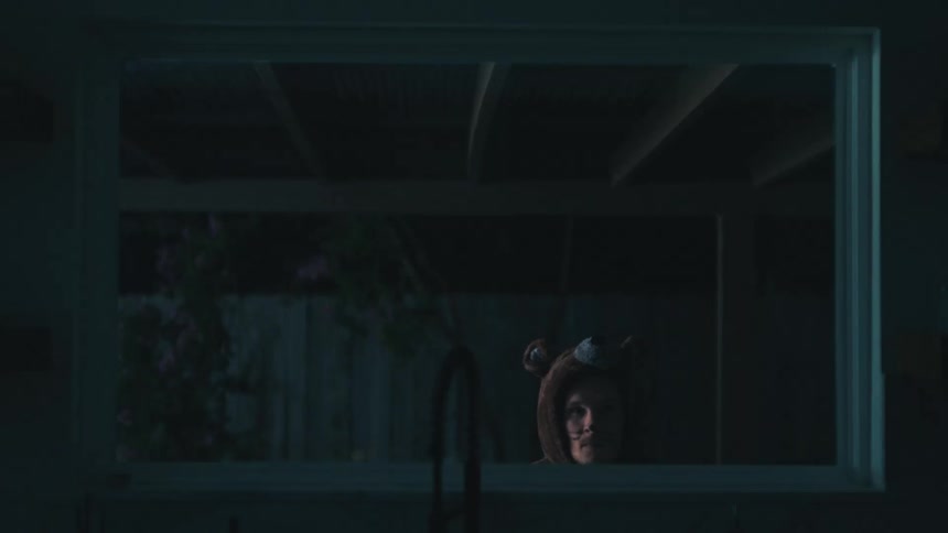 A man in a bear costume peeks his head up to look in the window