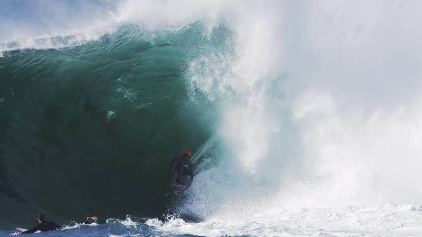 A man surfing a big wave and another man lying on the board next to the wave